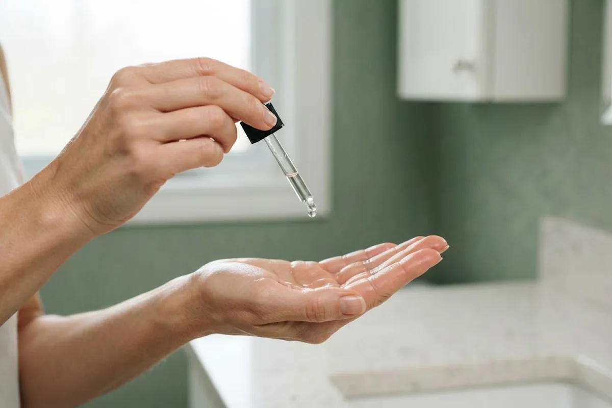 Hand holding a glass dropper over the palm with a clear serum, bathroom counter in Irvine CA