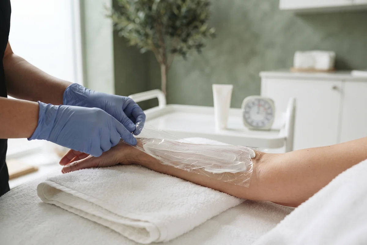 Topical numbing cream spread on an adult forearm and covered with clear plastic wrap in an Irvine CA studio